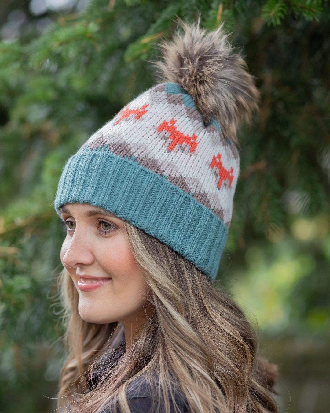 Woman wearing a knitted beanie with a pom-pom against a blurred green background.