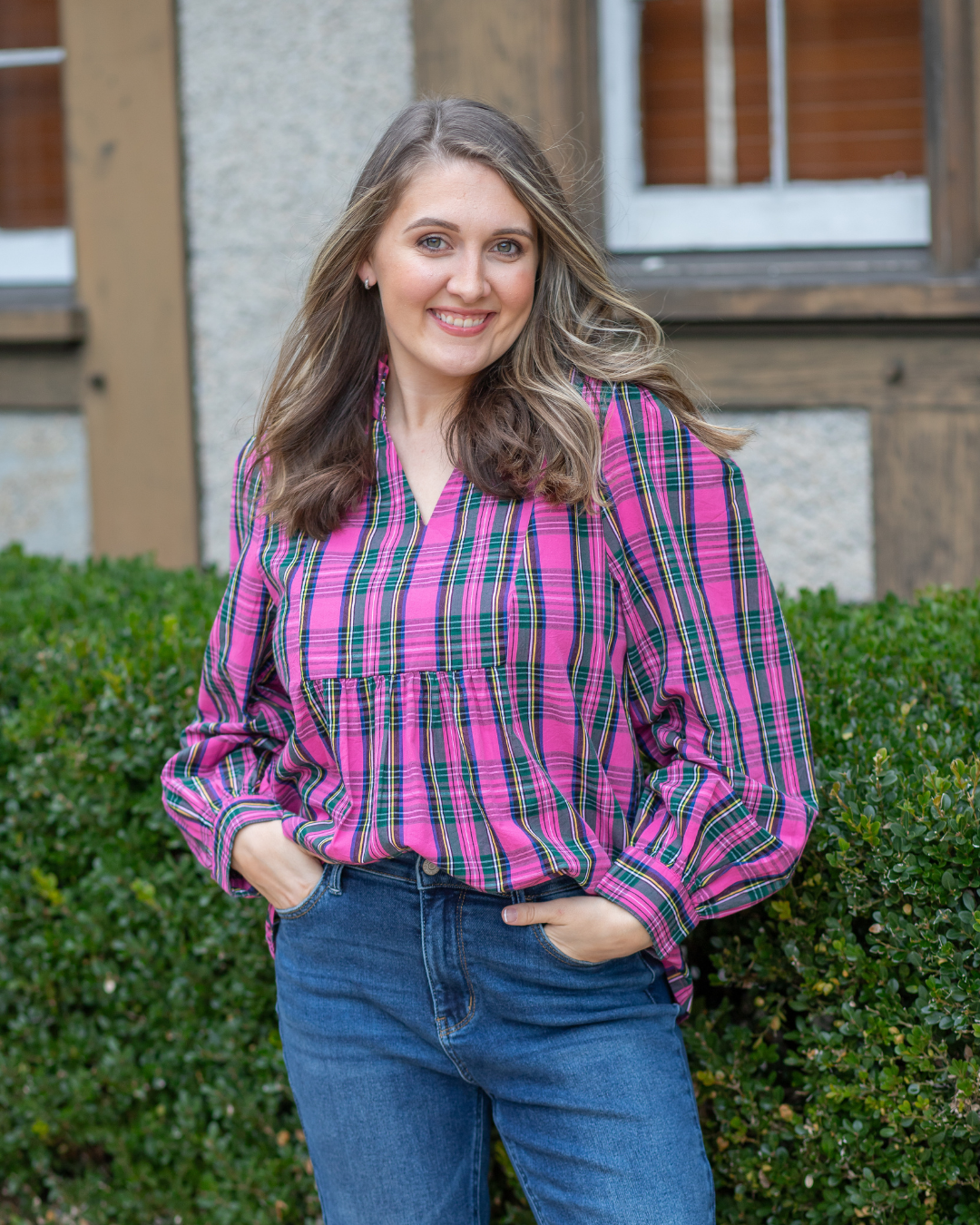 Woman wearing a pink and green plaid shirt standing in front of a building.