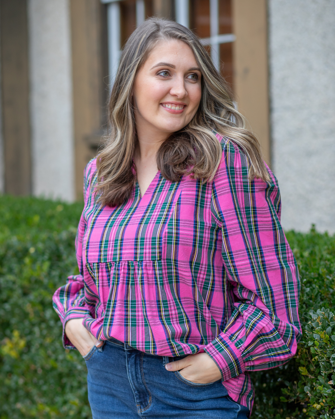 Woman wearing a pink and green plaid shirt standing outdoors..