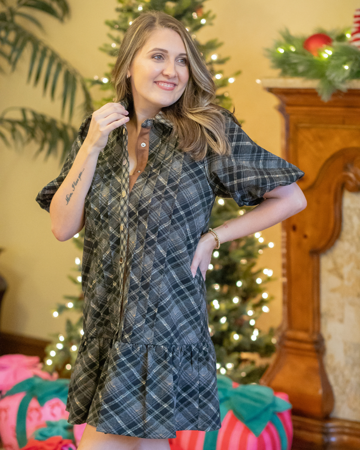 Woman wearing a plaid dress in a festive indoor setting with Christmas decorations.