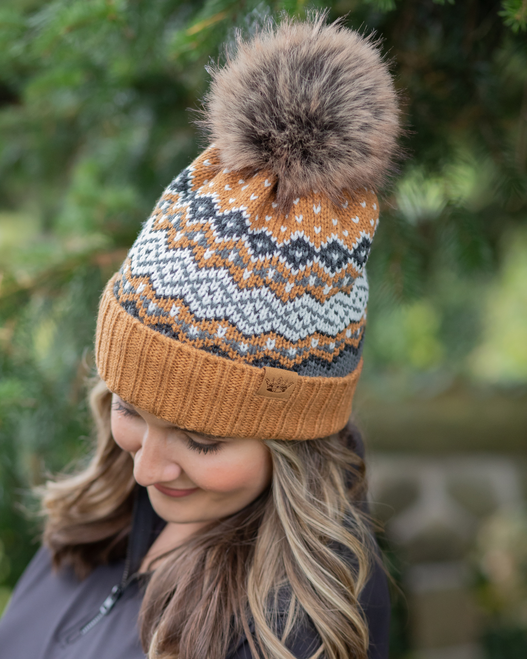 Person wearing a patterned knit hat with a fur pom-pom outdoors.