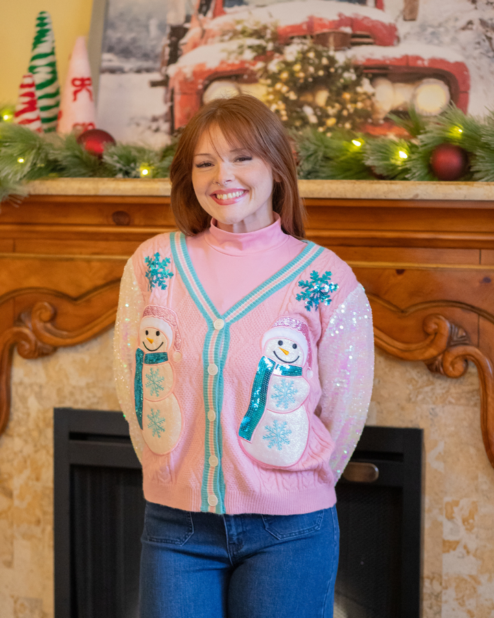 Woman wearing a pink sweater with snowman designs in front of a decorated fireplace.